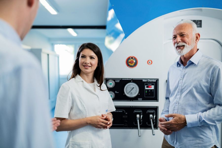 Paciente adulto mayor junto a una cámara hiperbárica durante una sesión de oxigenoterapia